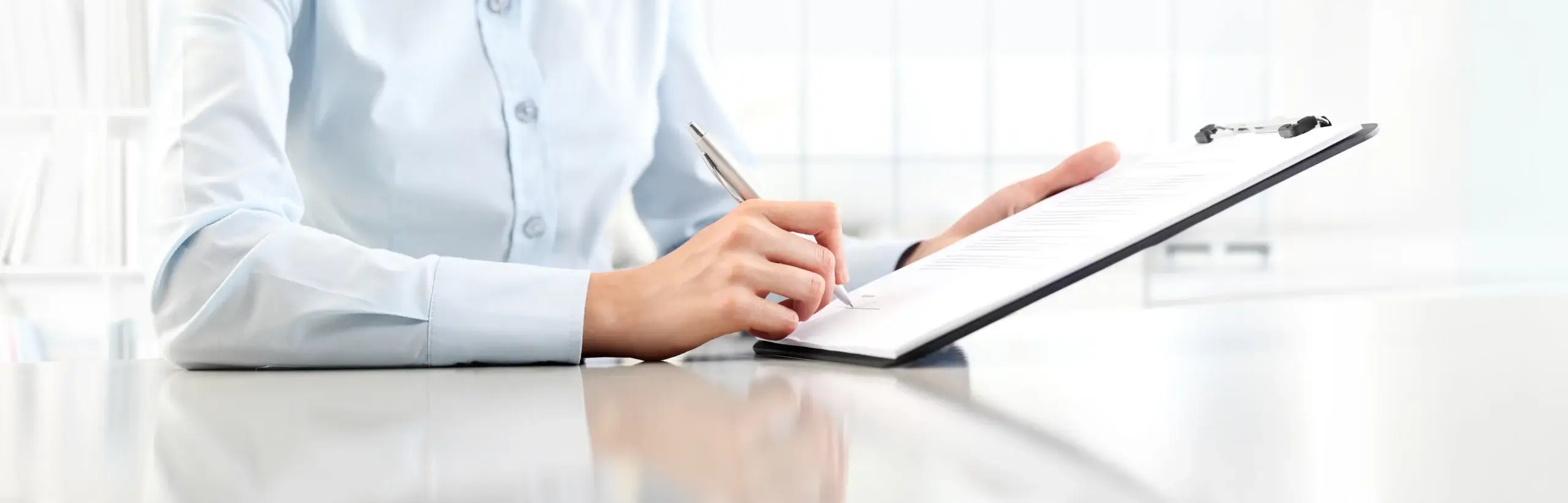 Woman's hands writing on sheet in a clipboard with a pen, isolated on desk